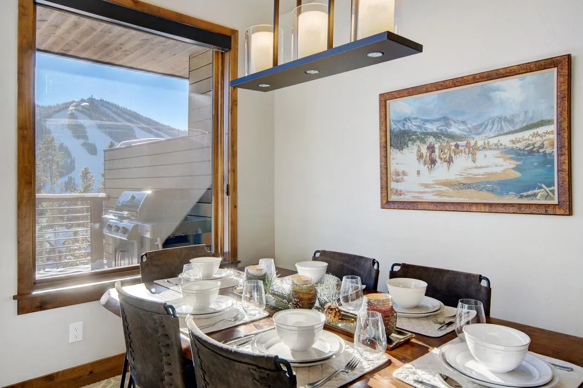 A dining table elegantly set for a meal, positioned in a sunlit corner with panoramic mountain views through large windows. Artwork on the wall adds a touch of personality, and the ambiance is warm and welcoming, perfect for both festive feasts and tranquil breakfasts.