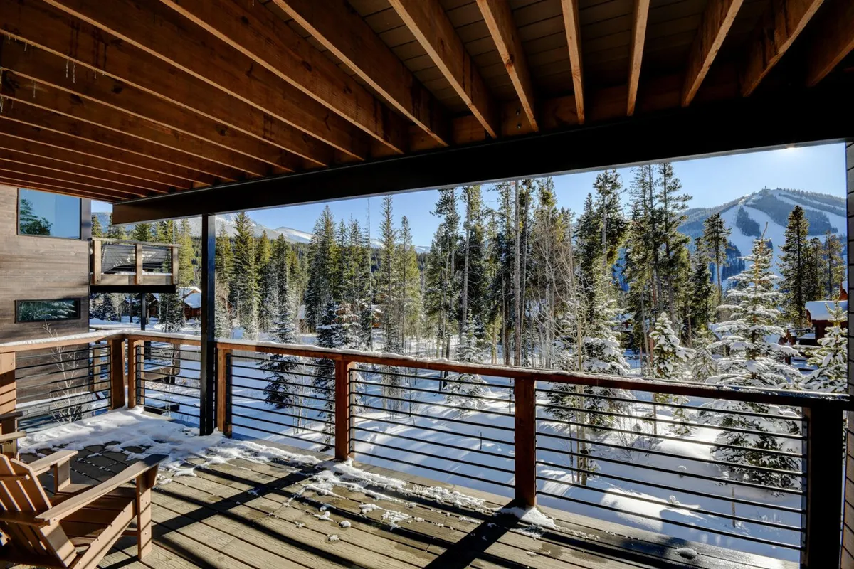 This image features a large wooden deck overlooking a snow-covered landscape with mountain vistas and trees. The deck provides ample space for outdoor gatherings, morning coffee, or evening drinks, as described in the section. The serene and peaceful setting is highlighted by the mountain backdrop.