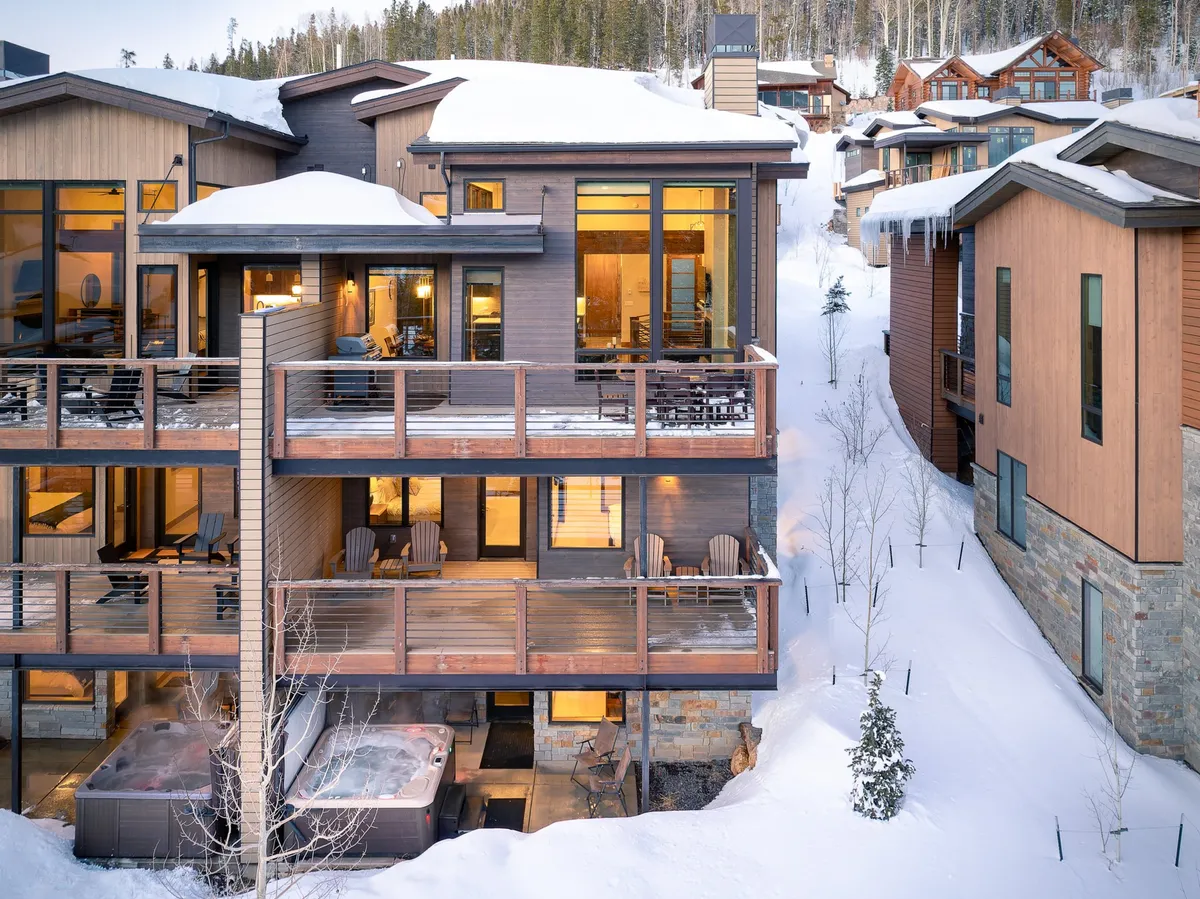 This exterior image showcases several balconies with inviting seating areas, hot tubs, and large windows, all set against a backdrop that hints at mountain views. The scene evokes a sense of gathering and relaxation, suggesting spaces ideal for group barbecues, evening chats, and shared experiences while connecting with the outdoors.