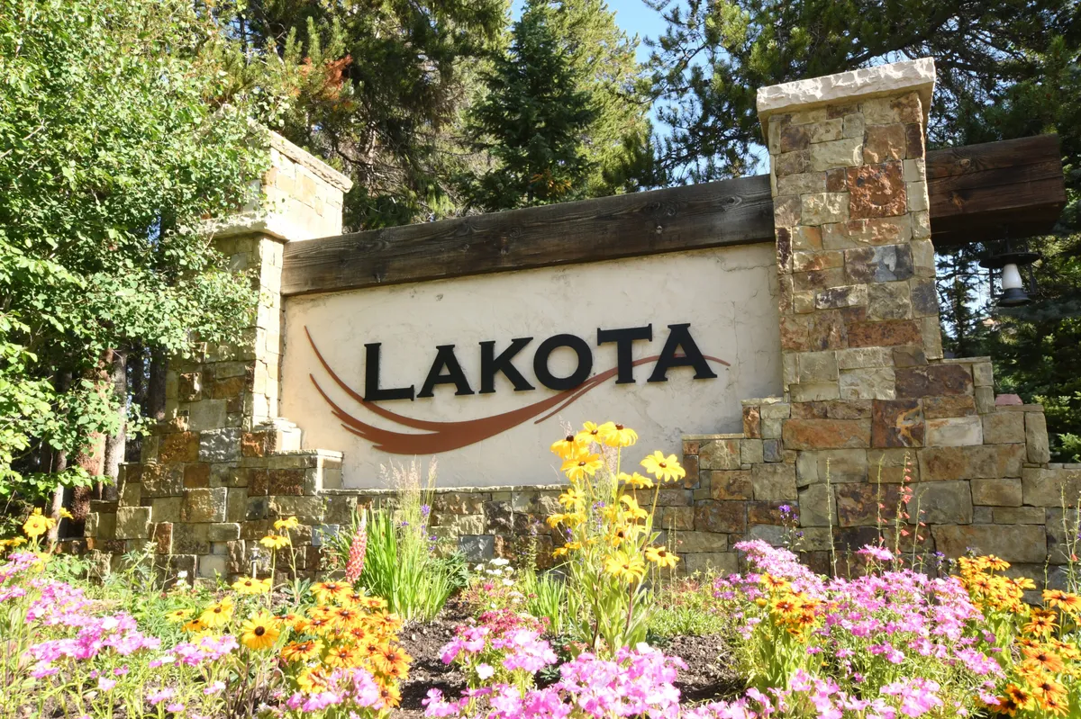 An inviting exterior shot featuring property signage nestled amidst colorful flowers and detailed stonework, creating a welcoming first impression. The garden area hints at the transition from the comfort of home to the beauty of the outdoors, suggesting a harmonious blend of nature and living space.