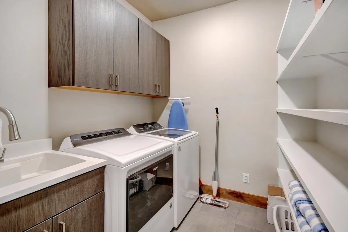 A calm and organized laundry room featuring a washing machine, dryer, sink, cabinets, and shelves. The space is tidy and functional, designed for handling laundry and organizing gear after outdoor adventures.