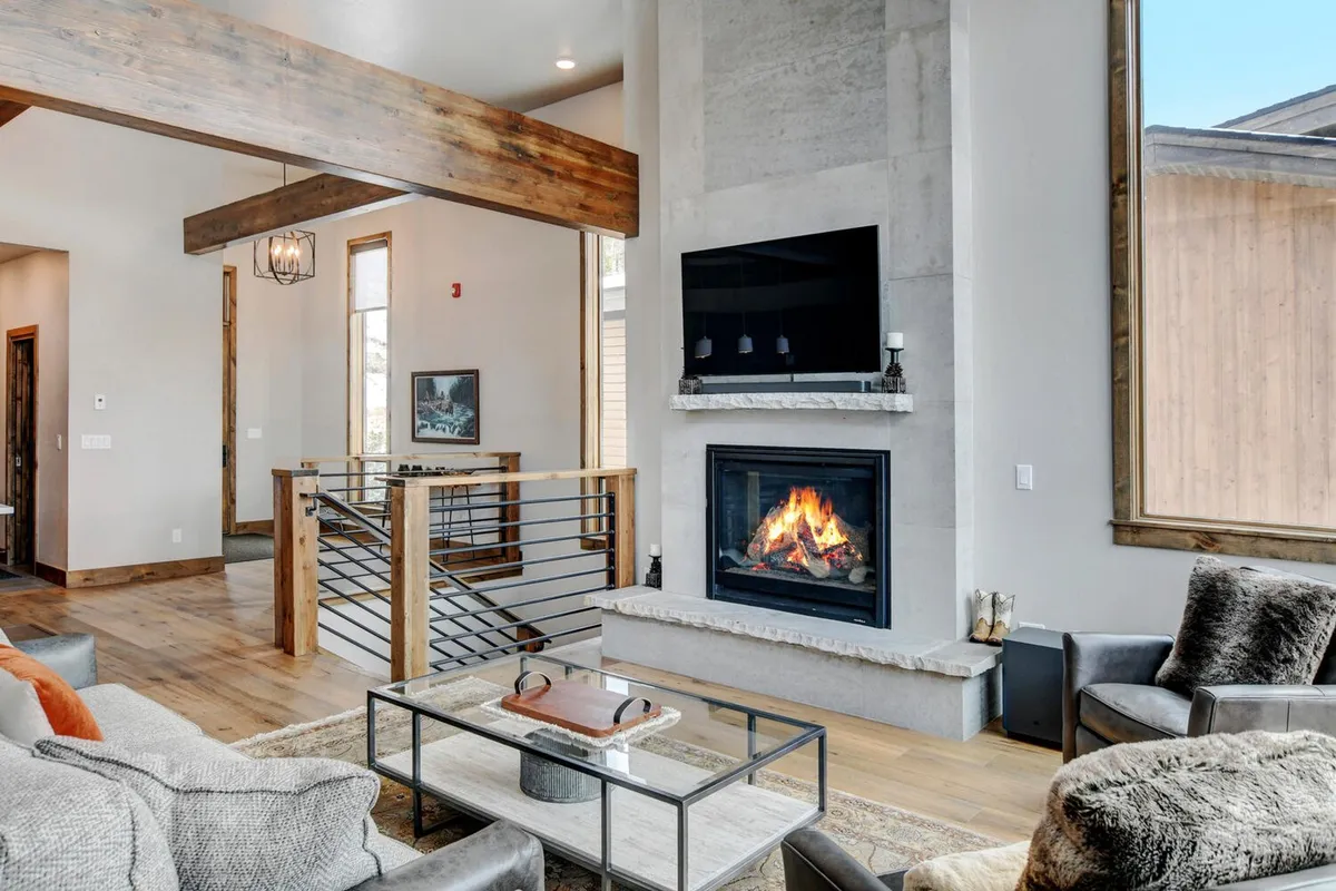 A warm, welcoming living area with a prominent fireplace, comfortable seating, large windows, wooden beams, and artwork on the wall. The space is ideal for relaxing with a book or drink after outdoor pursuits.